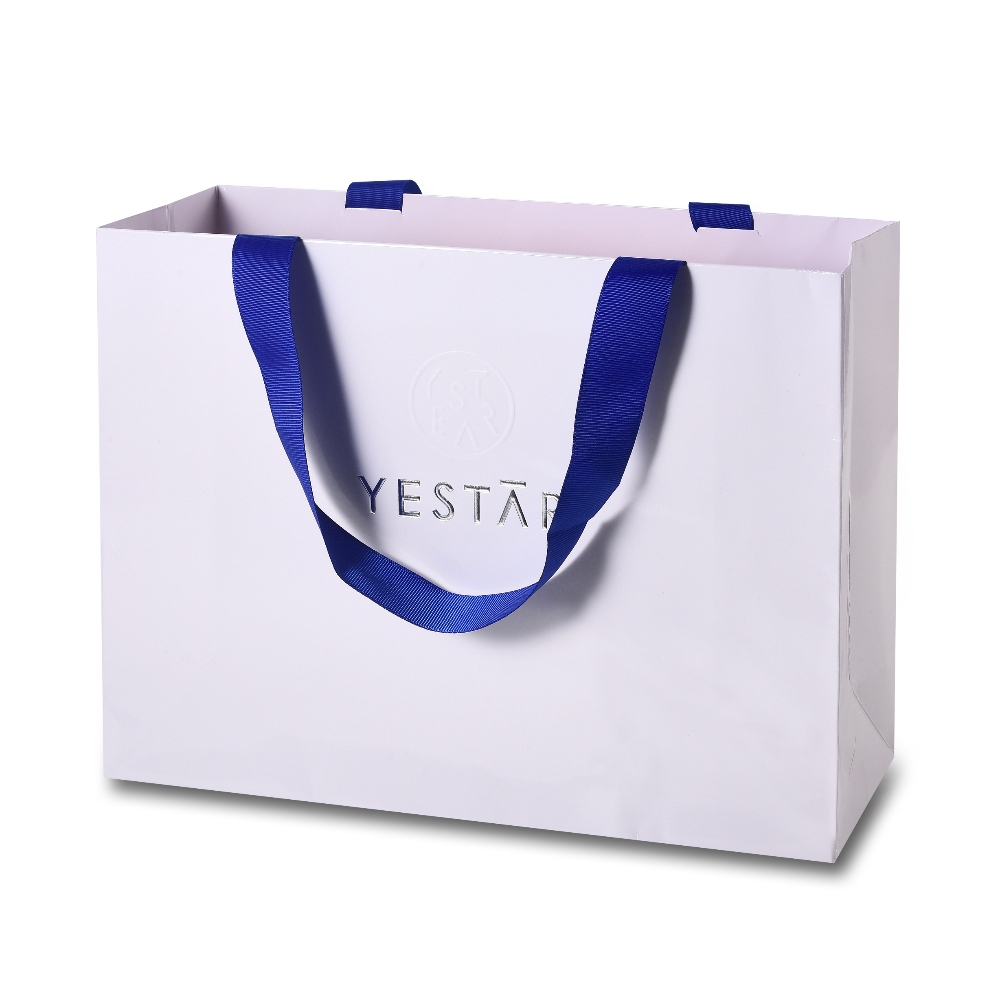 White laminated paper shopping bag with blue ribbon handles and debossed silver logo, luxury branded retail packaging bag.